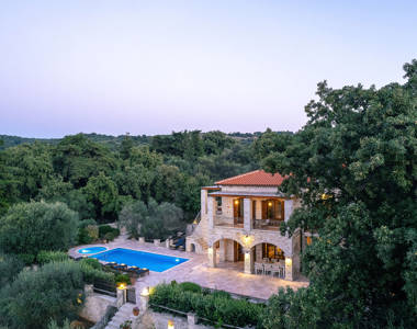 Vederi Estate Villa Melpomeni landscape view of the lit up villa exterior at dusk